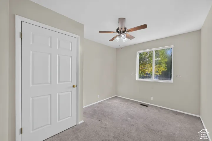 Room featuring neutral wall paint, carpeted flooring, a multi-panel interior door, a sliding window, and a ceiling fan with integrated lighting