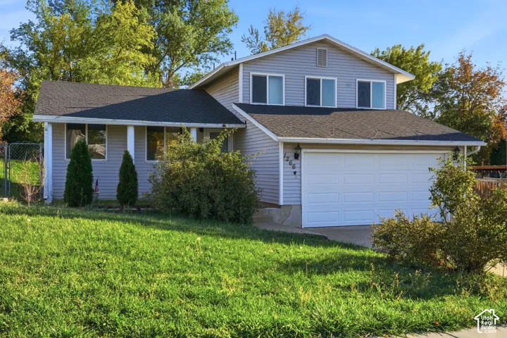 Split-level residence featuring horizontal vinyl siding, an attached two-car garage, asphalt shingle roofing, and a concrete driveway