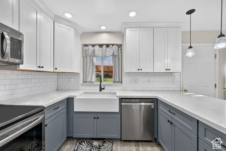 Kitchen featuring two-tone shaker-style cabinetry, white subway tile backsplash, quartz countertops, farmhouse-style apron sink, and stainless steel appliances