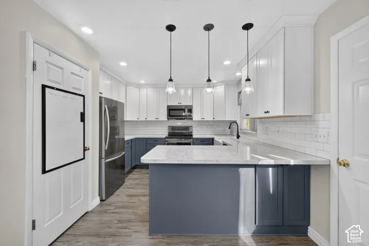 Kitchen featuring two-tone shaker cabinetry, quartz countertops, subway tile backsplash, stainless steel appliances, and three glass pendant lights