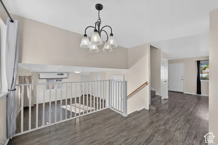 Wood-finish flooring, white metal balustrade railing, multi-light chandelier with frosted glass shades, and neutral wall tones