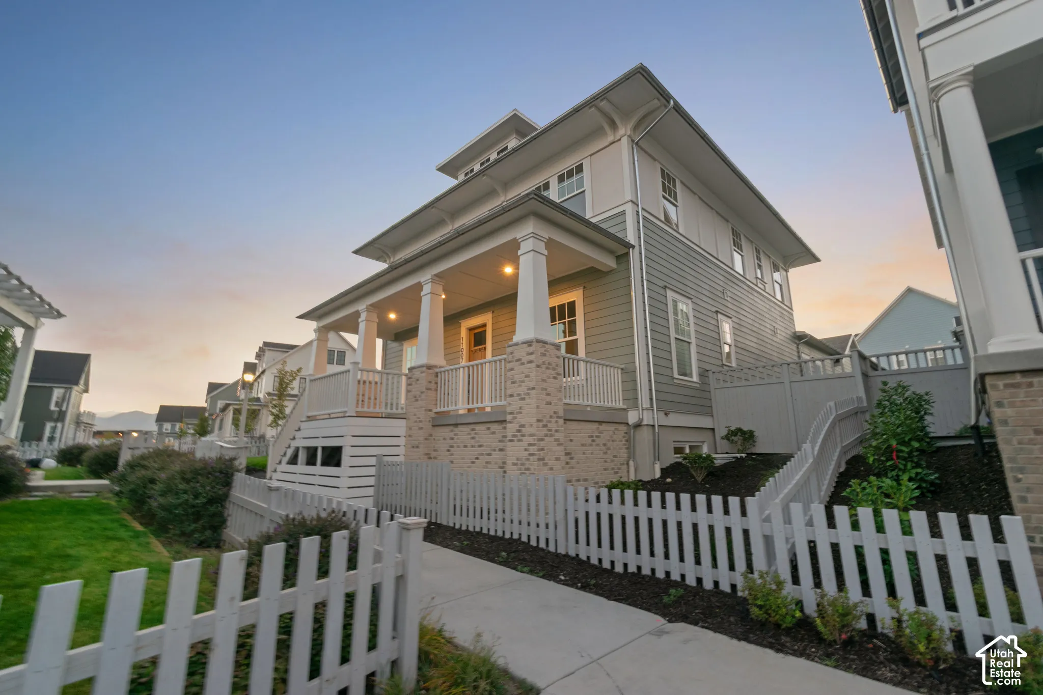 Exterior featuring horizontal lap siding, a covered front porch with square columns, brick pillar bases, and a white picket fence
