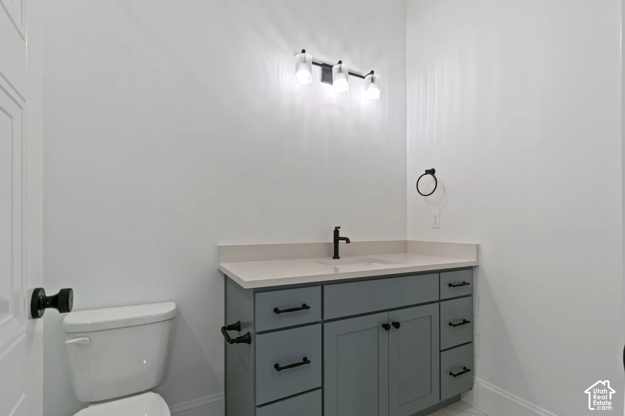 Grey shaker-style vanity with a solid surface countertop, rectangular undermount sink, matte black hardware, and a three-light fixture