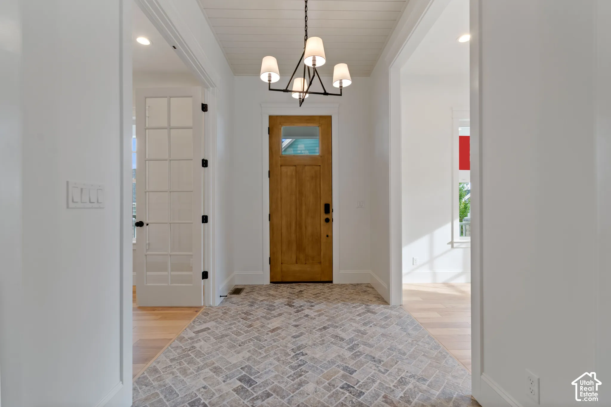 Foyer featuring herringbone-patterned stone flooring, wood-finish entry door with a glass inset, tongue-and-groove ceiling paneling, and a multi-arm geometric chandelier