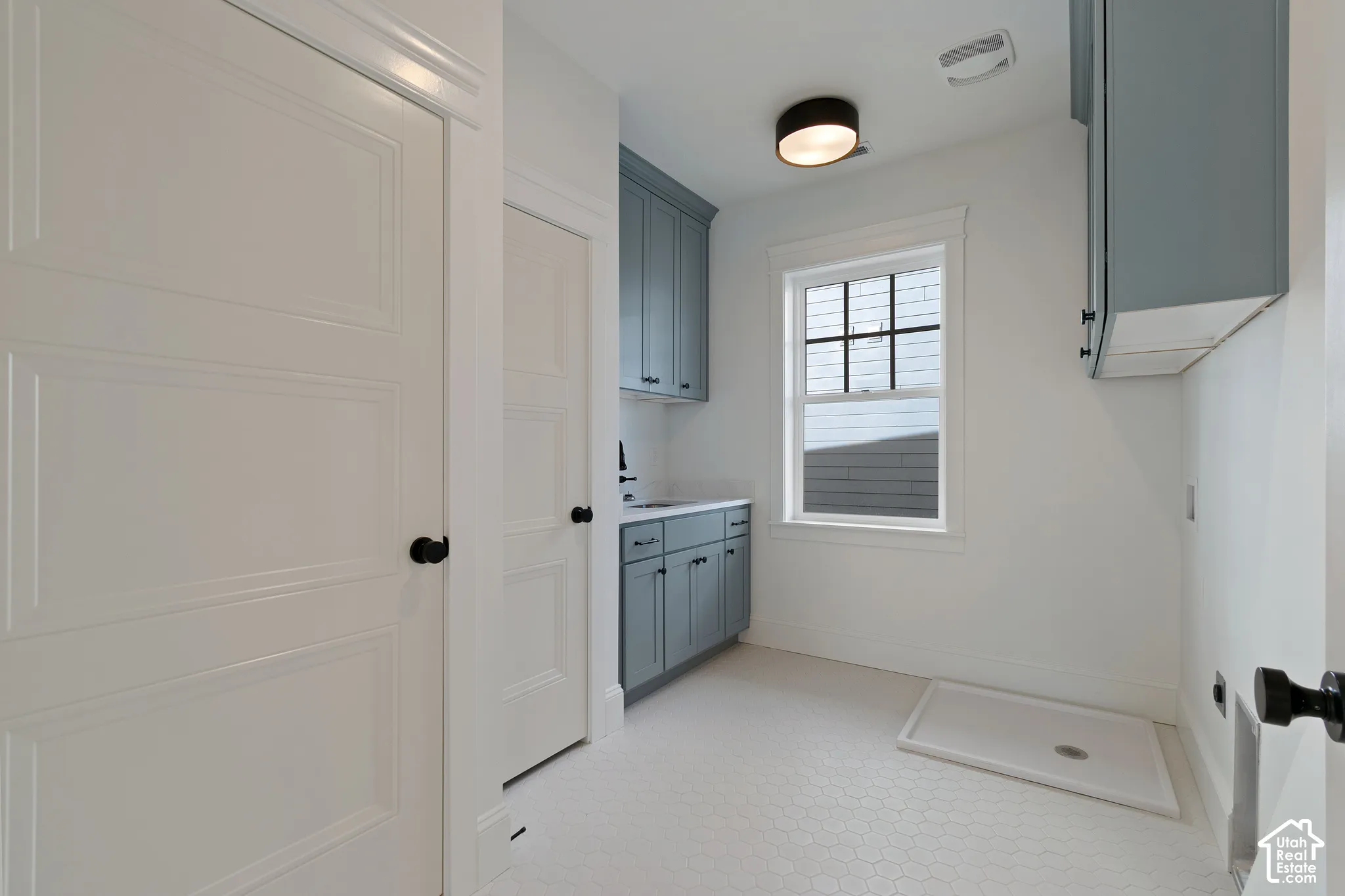 Blue-toned cabinetry featuring matte black hardware, integrated countertop with sink, white hexagonal floor tiling, and a window with a black grid frame