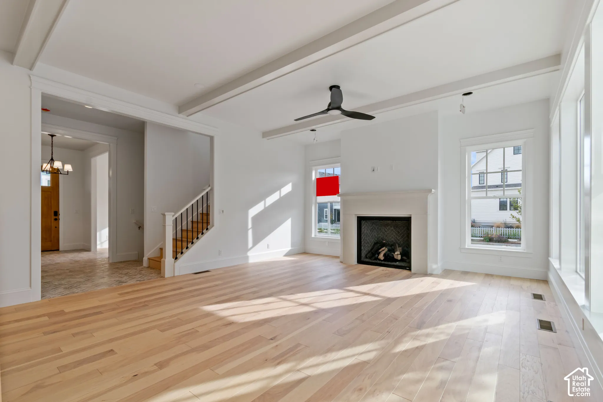 Light-toned wood-finish flooring, coffered ceiling detail, matte black ceiling fan, fireplace with a stone-finish mantle, and large-format multi-pane windows