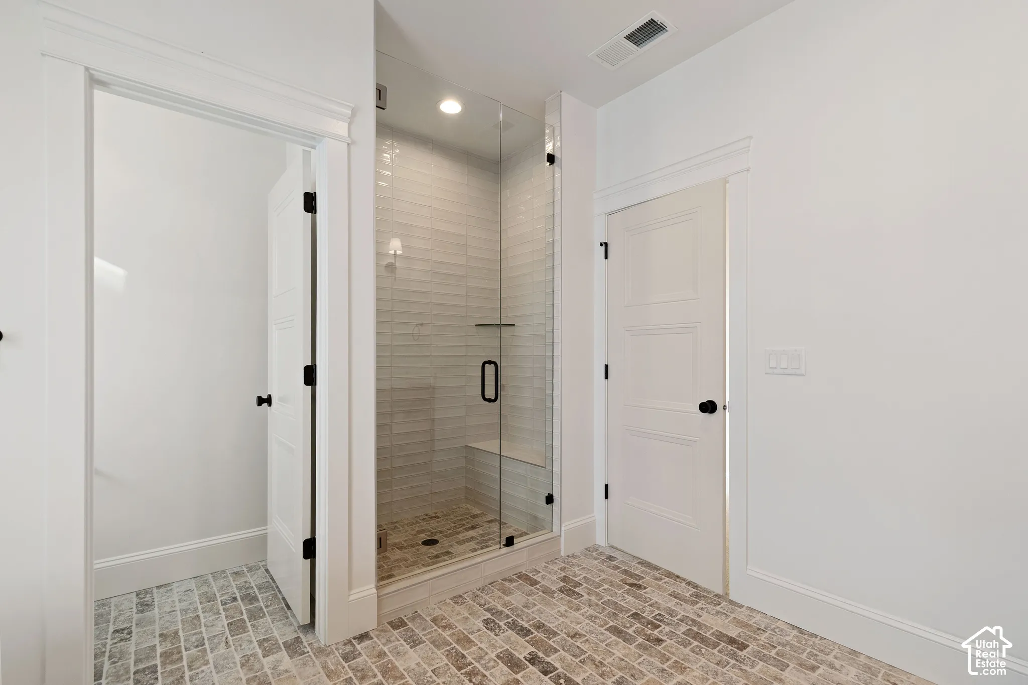 Walk-in shower featuring glass paneling, tile wall surround, integrated bench seating, and matte black hardware, set against stone-style flooring and paneled interior doors with matte black handles