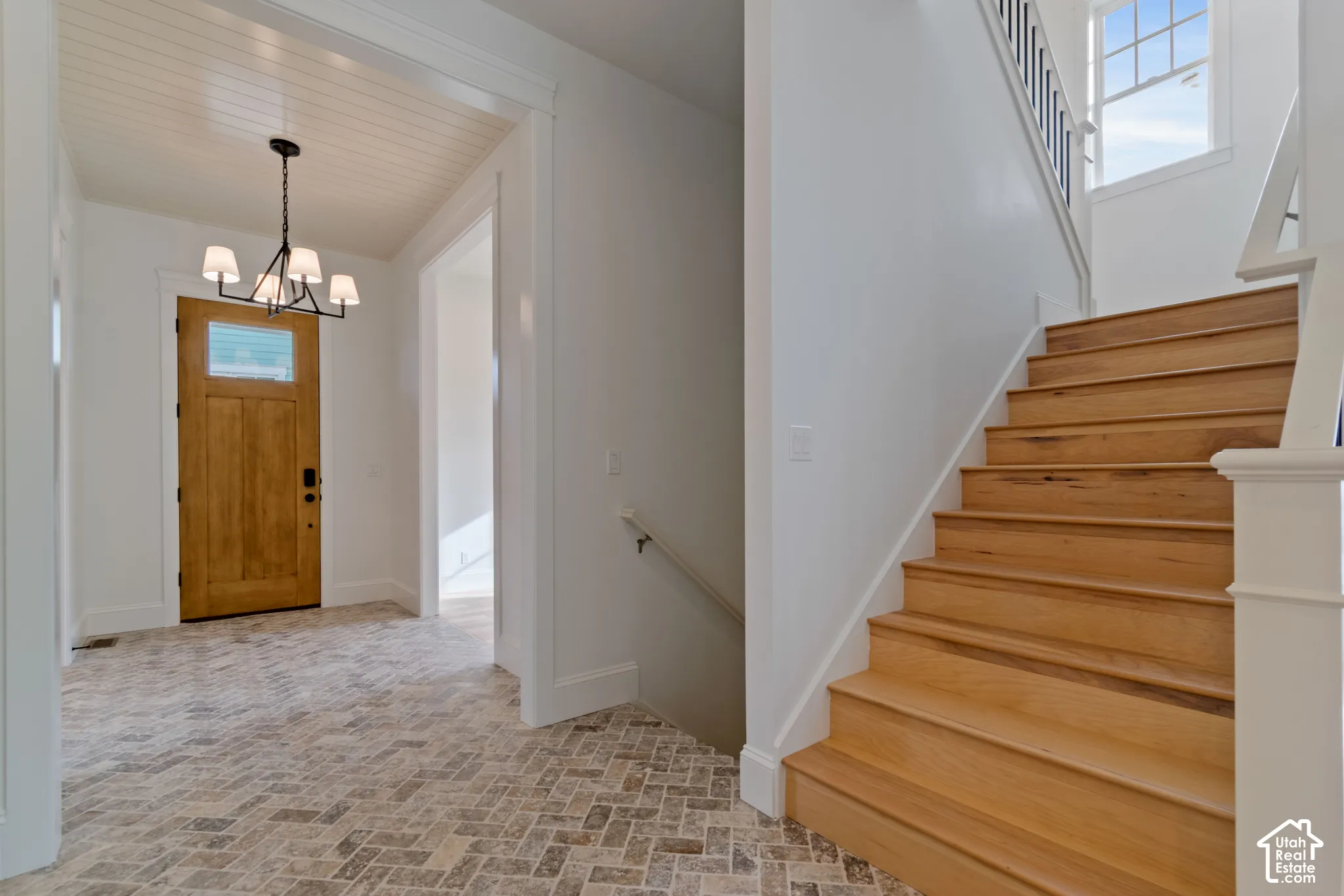 Foyer featuring herringbone-patterned stone flooring, wood-finish staircase with white millwork railing, beadboard ceiling detail, and a multi-arm chandelier