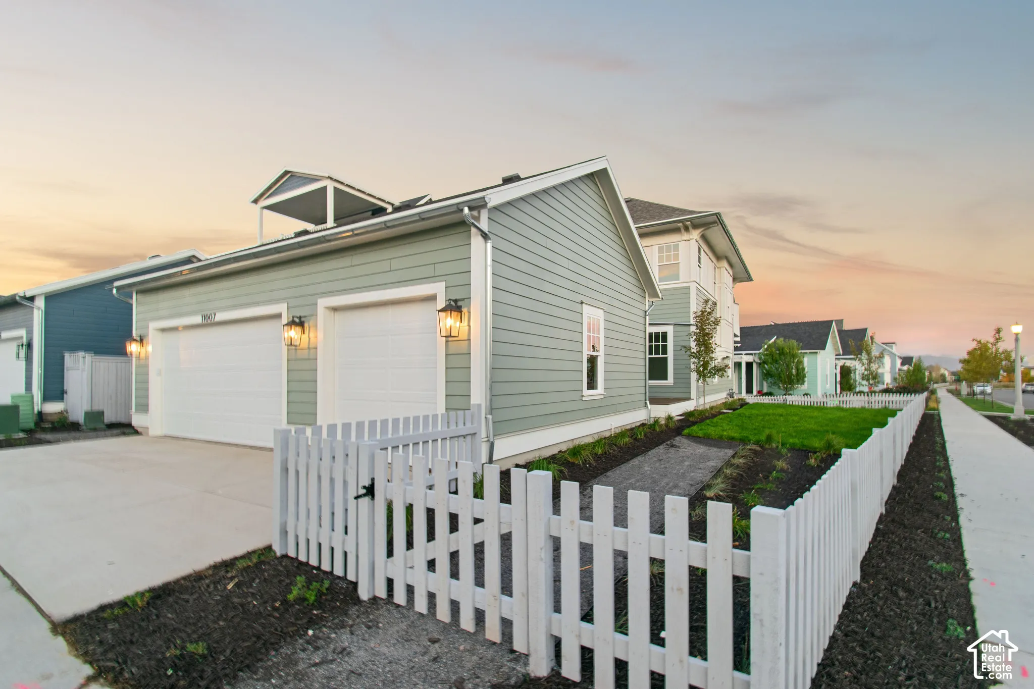 Two-car detached garage with horizontal siding, exterior wall-mounted lanterns, a white picket fence, and a concrete driveway