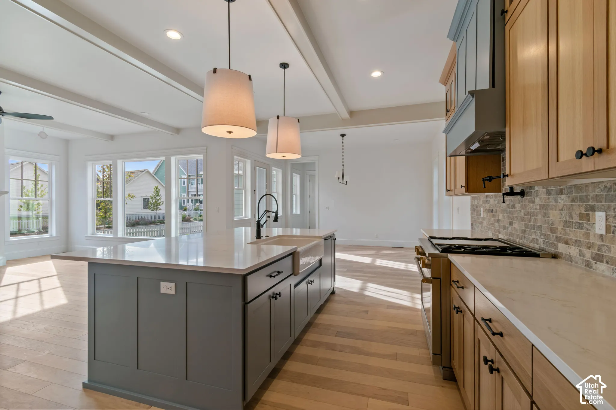 Kitchen featuring a center island with a farmhouse-style sink, quartz countertops, wood-finish flooring, stone-tiled backsplash, and recessed beam ceiling detailing