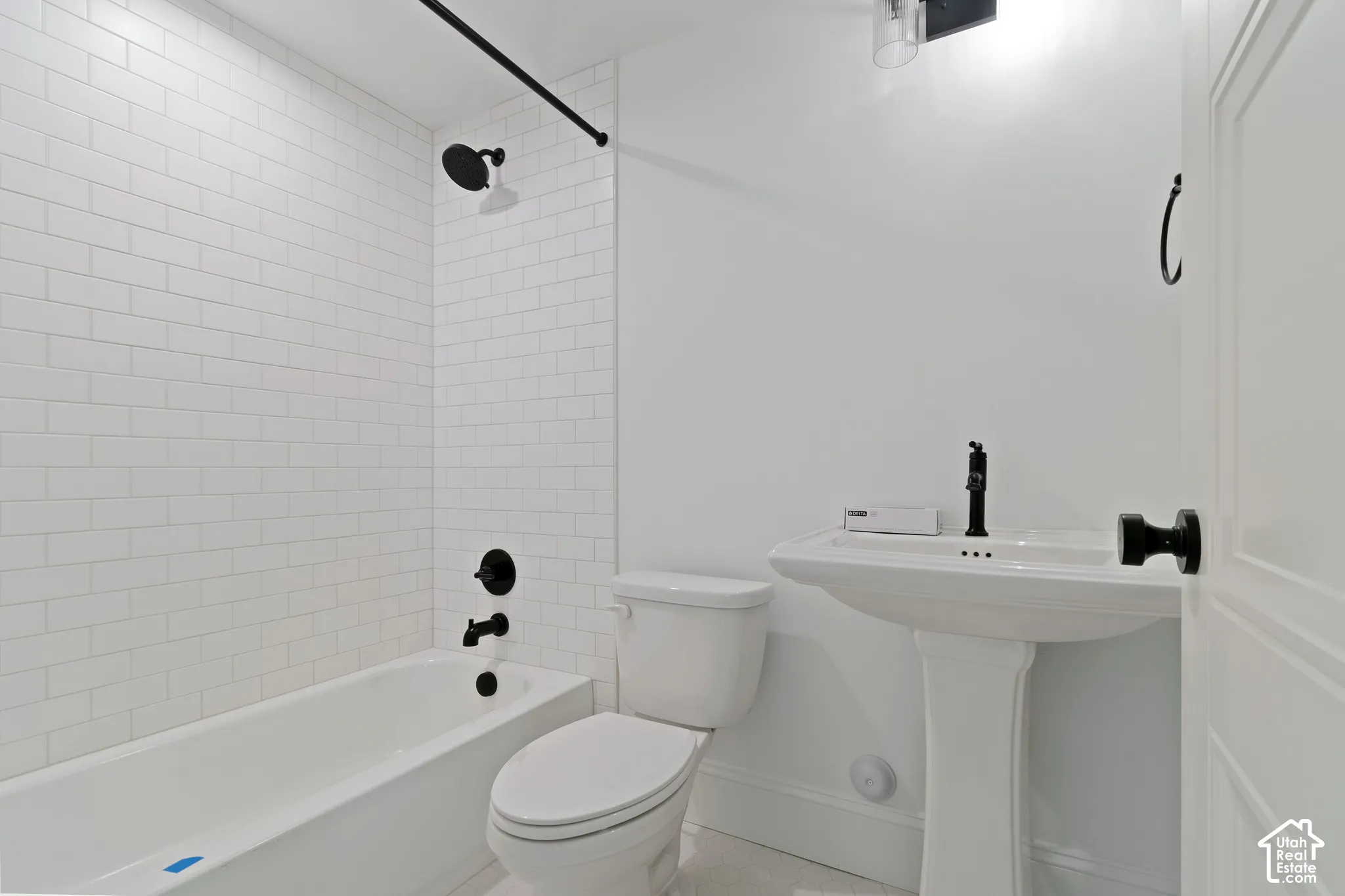 Bathroom featuring white subway tile tub surround, pedestal sink with matte black faucet, and matching matte black shower fixtures