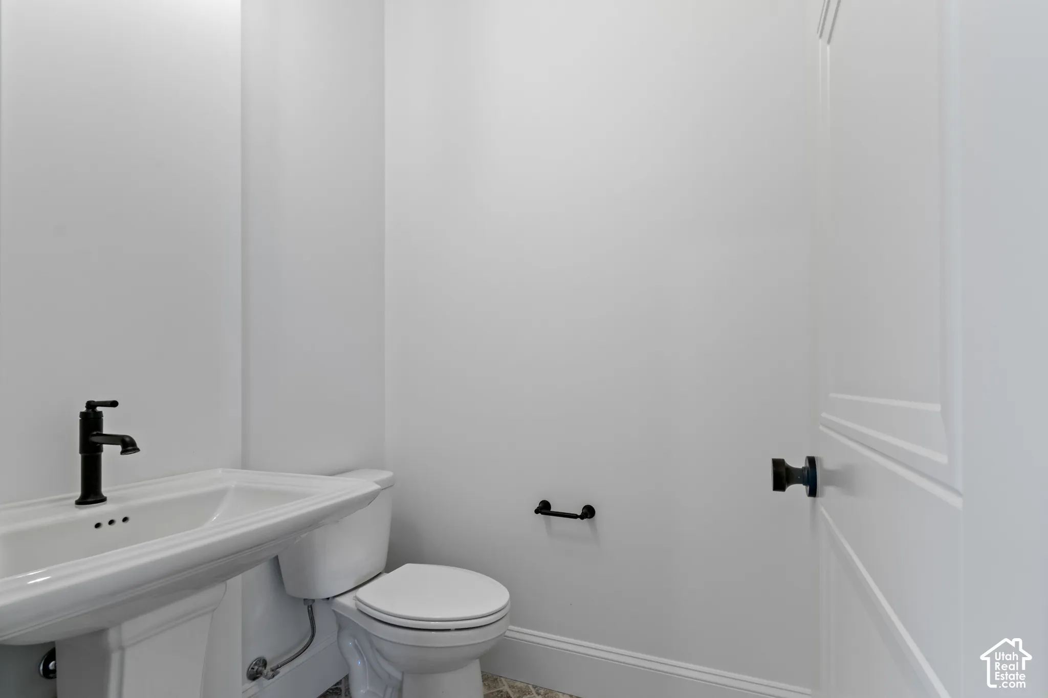 Pedestal sink with a matte black faucet, elongated toilet, matte black hardware, and patterned tile flooring