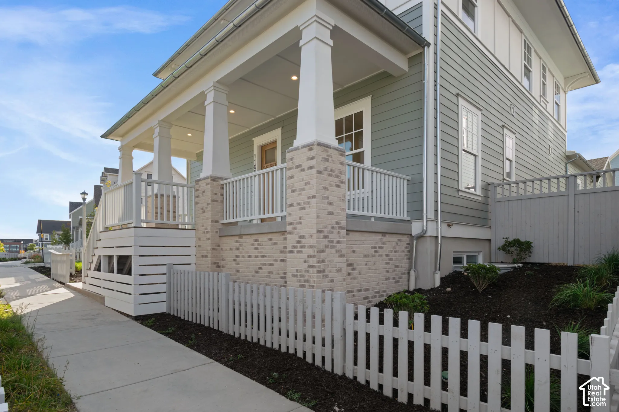 Craftsman-style exterior featuring horizontal siding, a covered porch with tapered columns, a brick foundation base, and a white picket fence