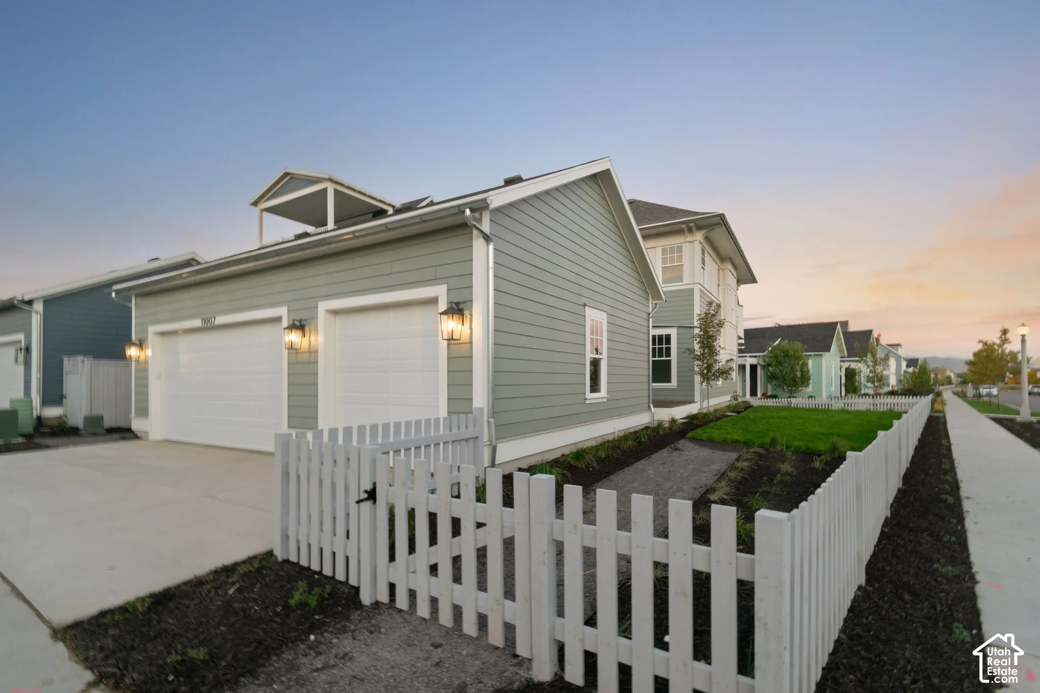 Exterior featuring horizontal lap siding, attached two-car garage, white picket fencing, and a small upper-level balcony