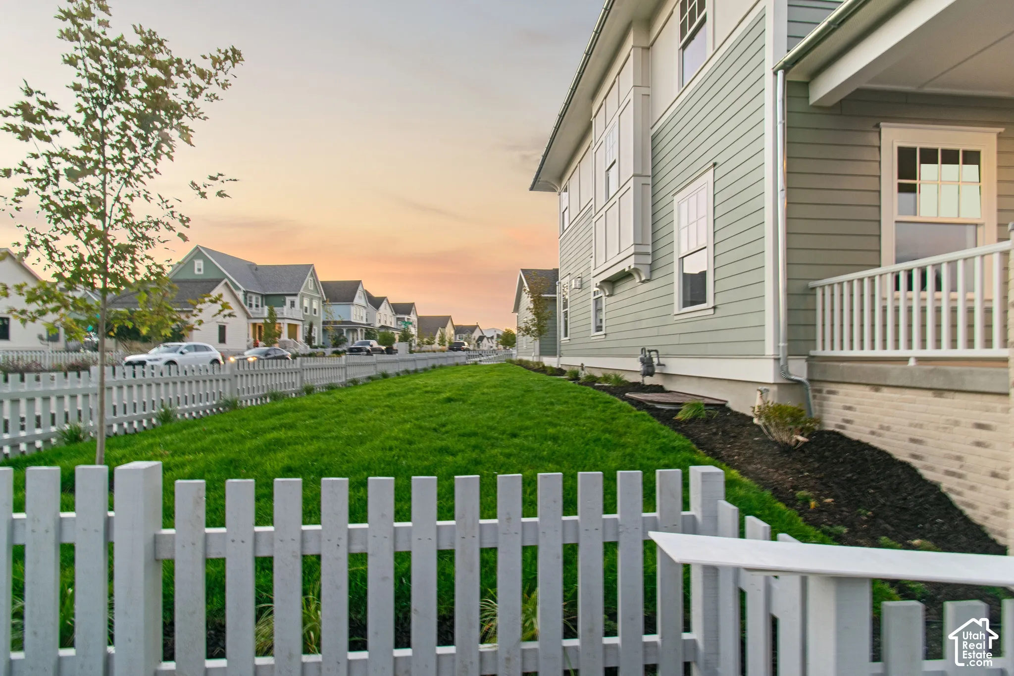 Exterior featuring horizontal lap siding, a covered porch with white railing, brick foundation veneer, and a white picket fence enclosing a manicured lawn
