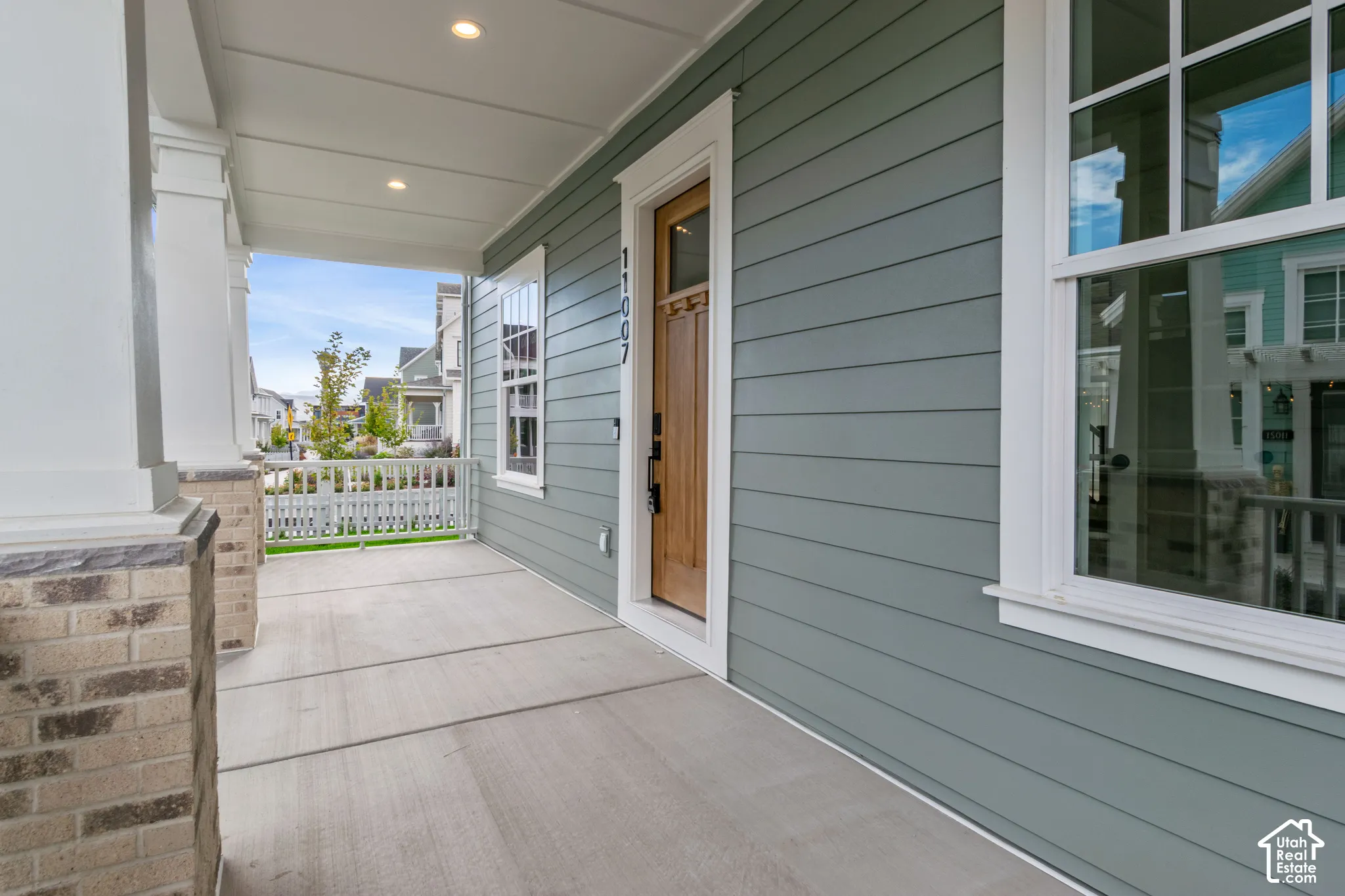 Covered front porch featuring horizontal lap siding, stone-base columns, a wood-finish entry door, and recessed lighting