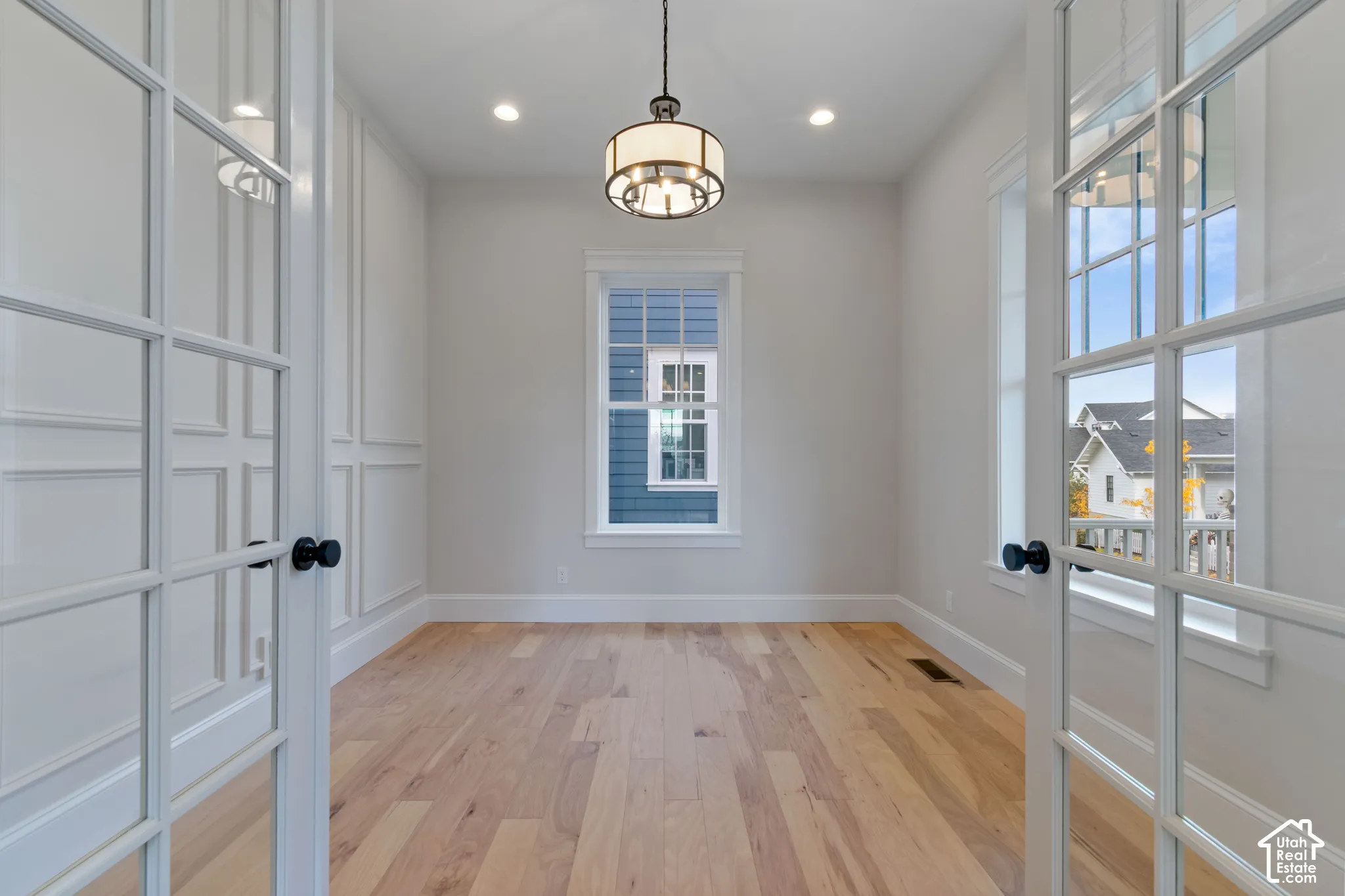 Interior room featuring wood-finish flooring, white French doors, decorative wall molding, a tiered drum pendant light, and multi-pane windows