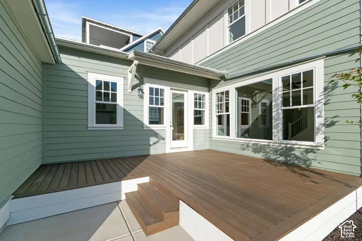 Exterior patio featuring horizontal lap siding, multi-pane windows, a glass-panel door, and a raised wooden deck with integrated steps