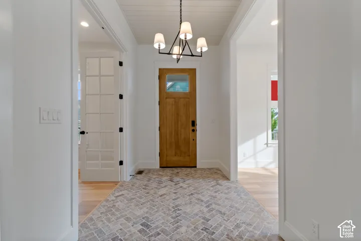 Foyer featuring herringbone-patterned stone flooring, wood-finish entry door with a glass inset, tongue-and-groove ceiling paneling, and a multi-arm geometric chandelier