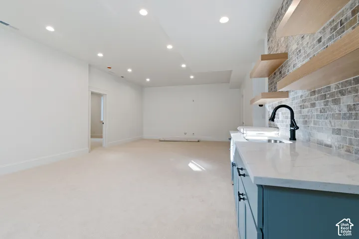 Interior featuring fitted cabinetry, a built-in sink, a gooseneck faucet, floating shelving, and a tiled accent wall