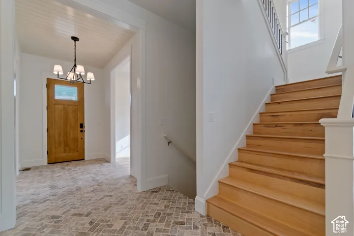 Foyer featuring herringbone-patterned stone flooring, wood-finish staircase with white millwork railing, beadboard ceiling detail, and a multi-arm chandelier