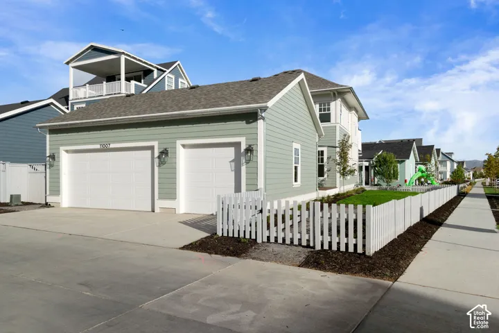 Exterior featuring horizontal lap siding, a two-car garage, concrete driveway, and a white picket fence enclosing a landscaped lawn