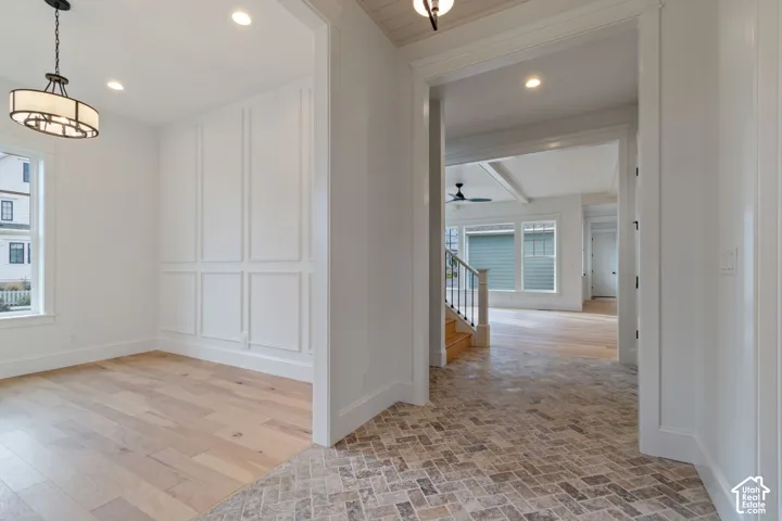 Herringbone-patterned stone flooring, wood-finish flooring, wainscot wall paneling, multi-tiered drum chandelier, and recessed lighting