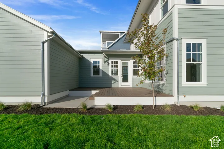Exterior featuring green horizontal siding, a raised deck, multi-pane windows, and a manicured lawn