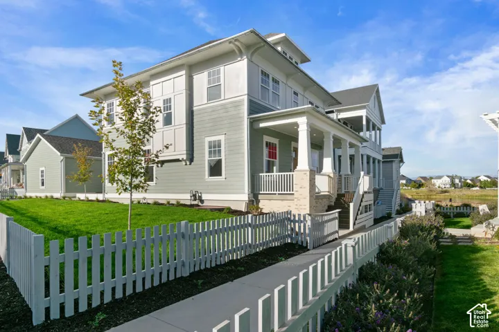 Multi-level exterior featuring light green horizontal siding, vertical board-and-batten accents, stone-base columns on the covered porch, and a white picket fence enclosing the manicured lawn