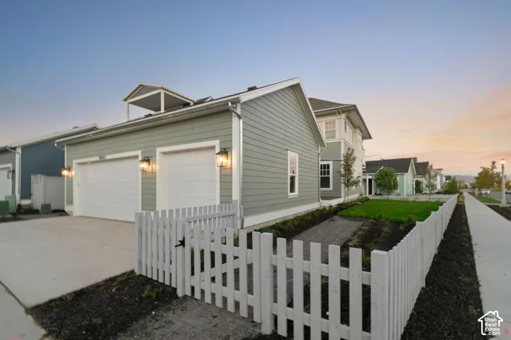 Exterior featuring horizontal lap siding, attached two-car garage, white picket fencing, and a small upper-level balcony
