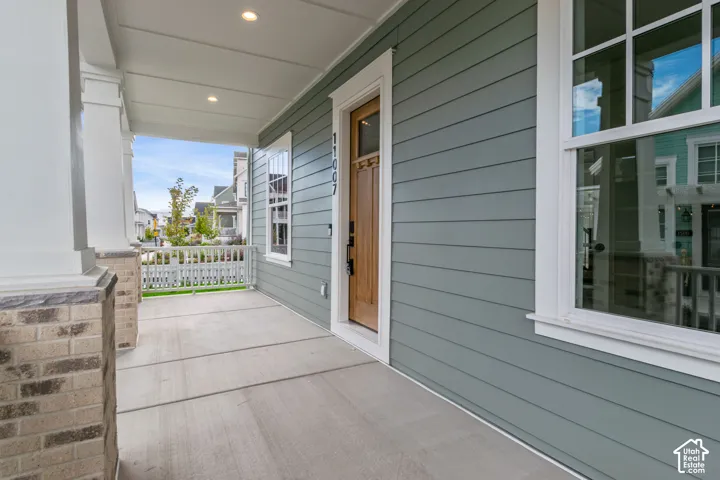 Covered front porch featuring horizontal lap siding, stone-base columns, a wood-finish entry door, and recessed lighting