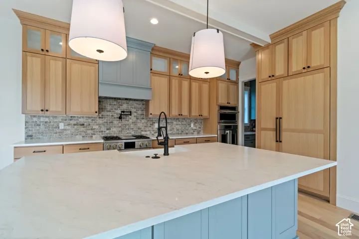 Kitchen featuring light wood-finish cabinetry, a large central island with quartz countertop, a brick backsplash, built-in panel-ready refrigeration, and a professional-style range with wall-mounted pot filler