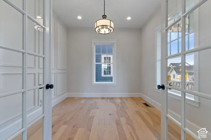 Interior room featuring wood-finish flooring, white French doors, decorative wall molding, a tiered drum pendant light, and multi-pane windows