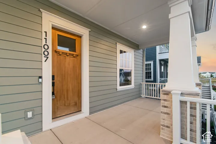 Covered front porch featuring horizontal lap siding, a wooden front door with an inset window, square structural columns, and a brick-based railing