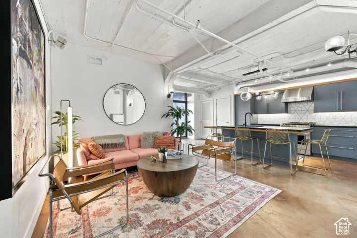 Polished concrete flooring, exposed ceiling ductwork, kitchen island with seating, stainless steel appliances, and a geometric tile backsplash