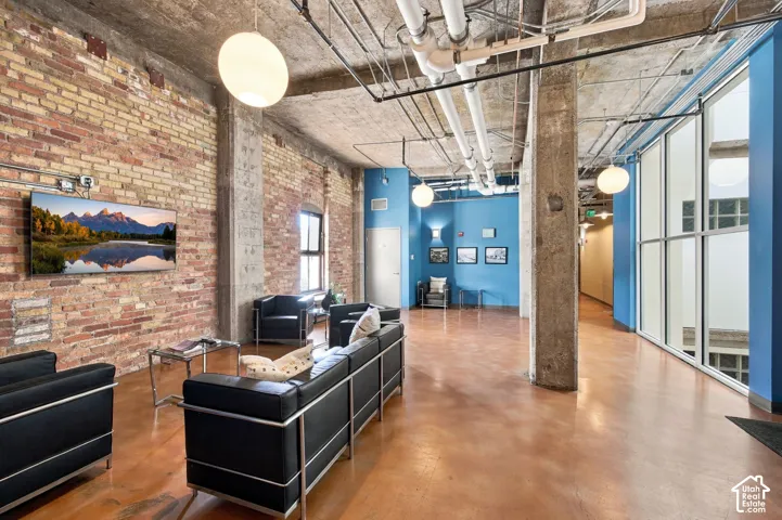 Exposed brick wall, concrete flooring, exposed ceiling pipes, pendant lighting, and full-height interior windows