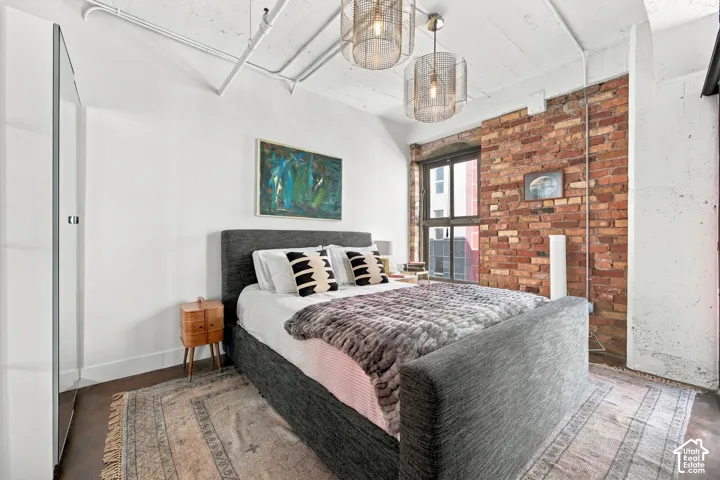 Exposed brick accent wall, high ceilings with visible conduit, large industrial-style window, and dual overhead pendant lighting