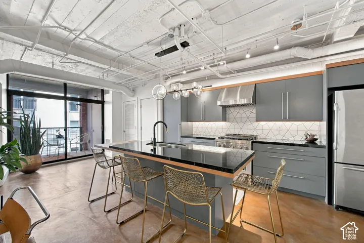 Modern kitchen featuring gray cabinetry, stainless steel appliances, a geometric tile backsplash, and an island with a black countertop