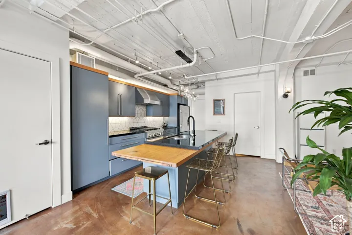 Modern kitchen featuring dark cabinetry, a black countertop island, and a light wood-finish breakfast bar