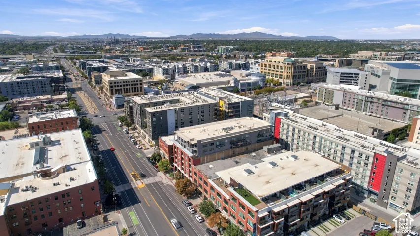 Aerial perspective showcasing urban density with multiple residential and commercial structures, paved roadways, and distant natural terrain