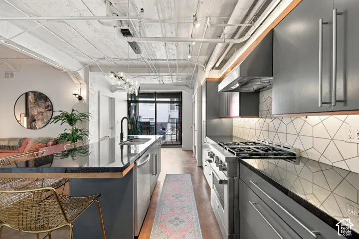Exposed ceiling conduits, contemporary kitchen cabinetry, stainless steel appliances, geometric tile backsplash, and a large kitchen island with an integrated sink