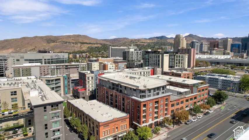 Urban skyline with varied architectural styles, including contemporary and traditional brick facades, set against a backdrop of distant mountains