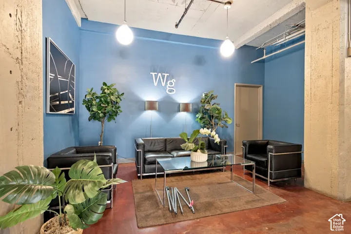 Exposed concrete column, high ceilings, pendant lighting, blue accent wall, and a concrete floor