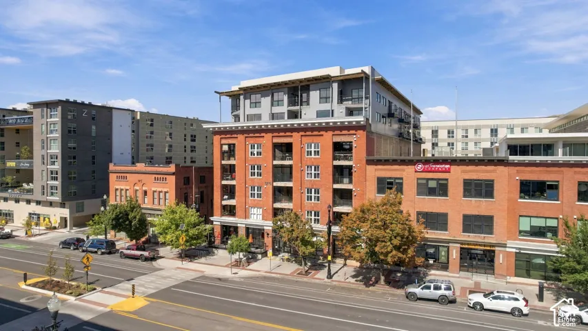 Brick facade building with multiple balconies and ground-floor retail spaces, featuring a contemporary upper level
