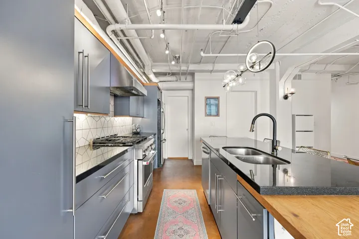 Kitchen featuring stainless steel appliances, grey cabinetry, a patterned tile backsplash, dark countertops, and a dual-basin sink with a matte black faucet