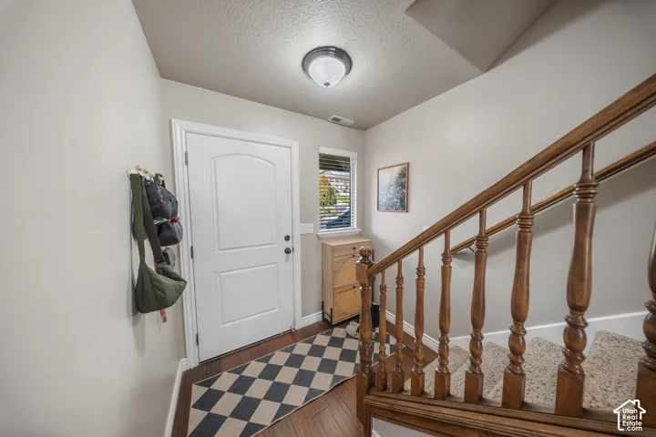 Entryway featuring a white paneled door, wood-finish flooring, a wood baluster staircase with carpeted steps, and a flush-mount ceiling light fixture