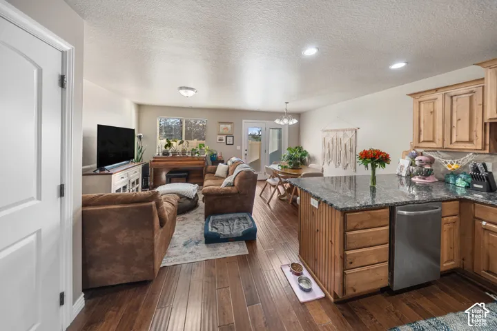 Kitchen featuring wood-finish flooring, stone-surface peninsula, stainless steel dishwasher, and wooden cabinetry with recessed lighting