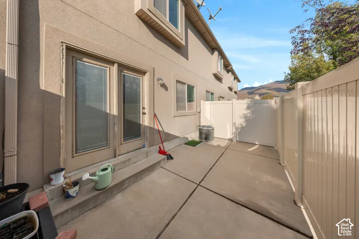 Stucco exterior featuring dual glass-paneled entry doors, a concrete patio, and a perimeter privacy fence with mountain surroundings
