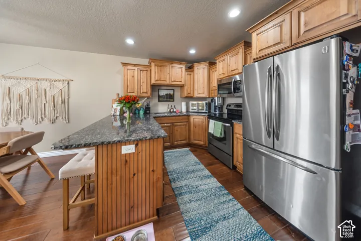 Kitchen featuring wood-finish cabinetry, stone-surface breakfast bar, stainless steel refrigerator, built-in microwave, and wood-finish flooring