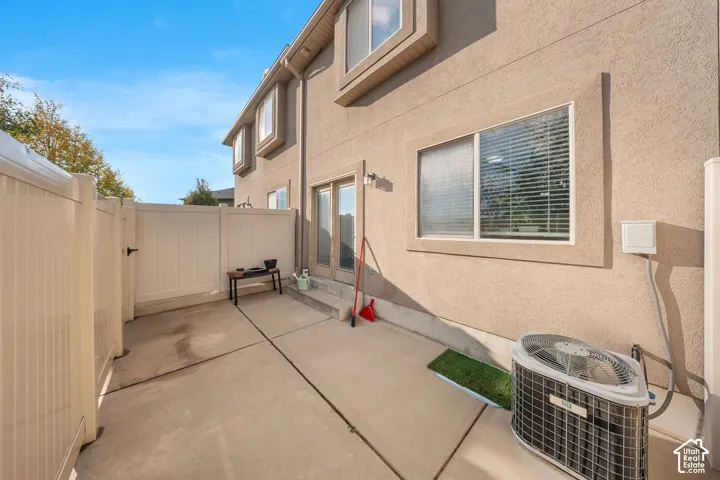 Stucco exterior featuring a concrete patio, white vinyl privacy fencing, and exterior central air conditioning unit